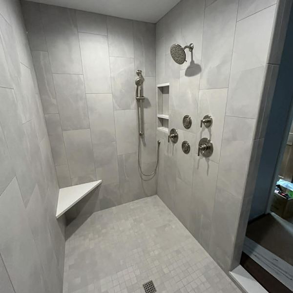 Custom tile shower with body sprays and a built-in bench by KW Plumbing