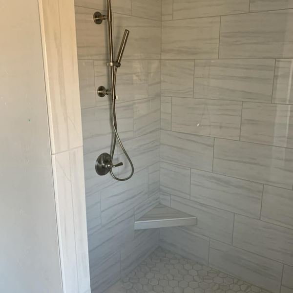 Tiled walk-in shower with corner bench and handheld shower by KW Plumbing
