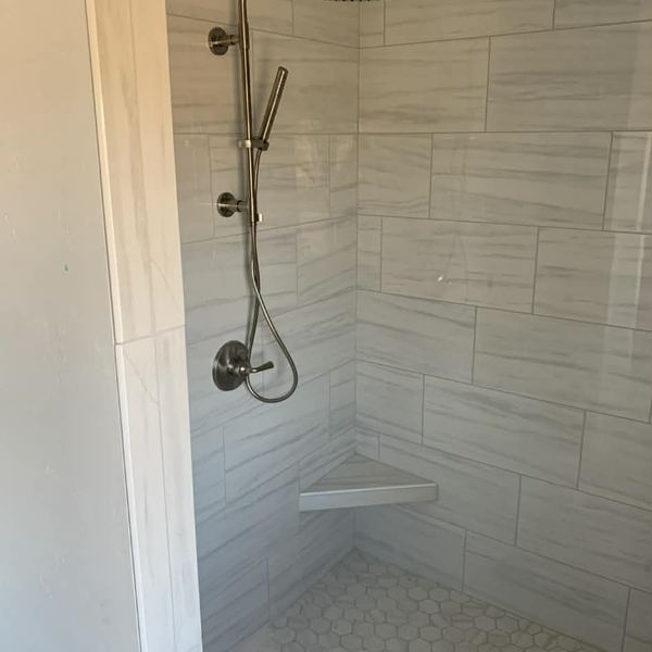 Tiled walk-in shower with corner seat by KW Plumbing